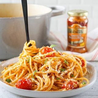 pesto pasta on a white plate with a black fork, a grey pot and pesto jar in the background