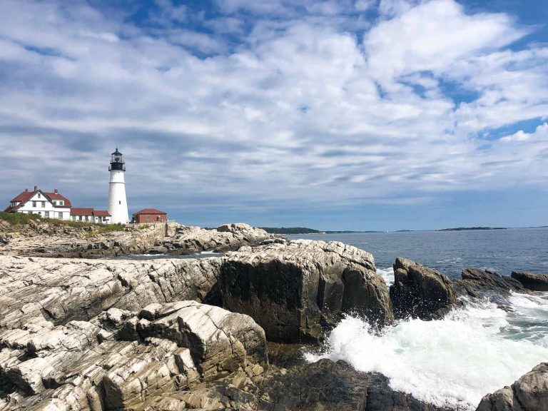 landscape photo of the portland head lighthouse with waves crashing on rocks