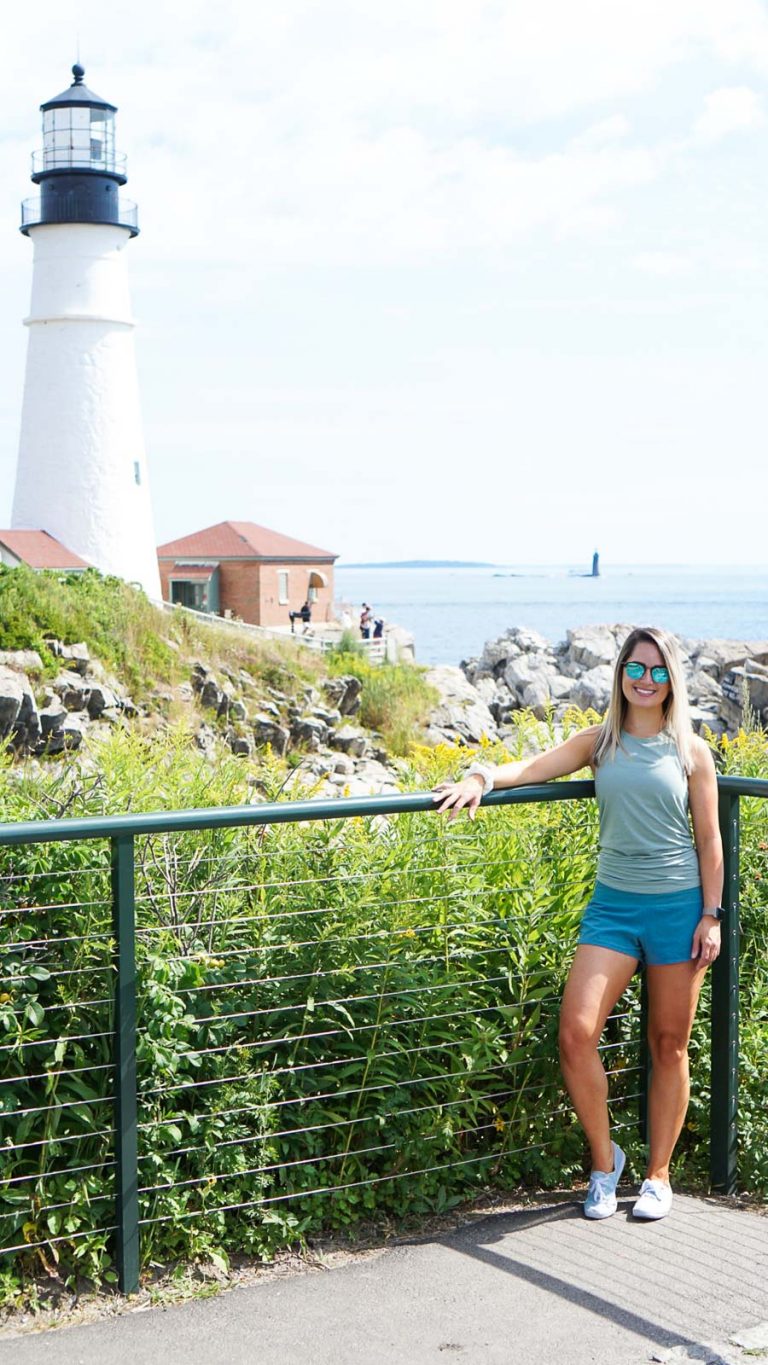 a girl with blonde hair standing against a railing with a lighthouse in the background