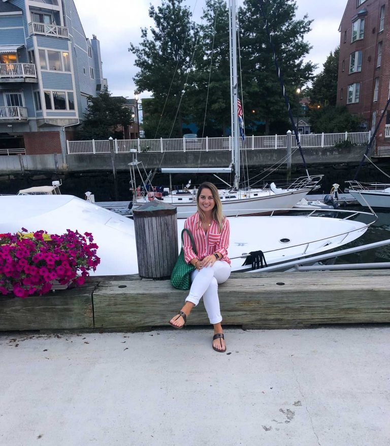 a girl sitting by a boat in white pants and a pink striped shirt