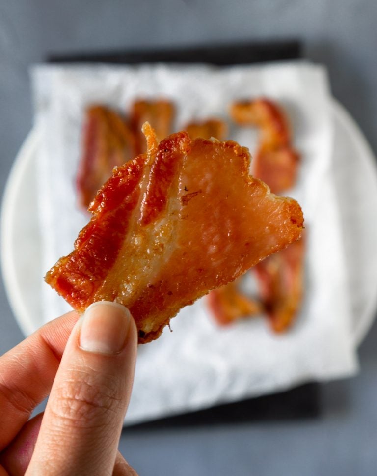 a hand holding a piece of air fryer bacon