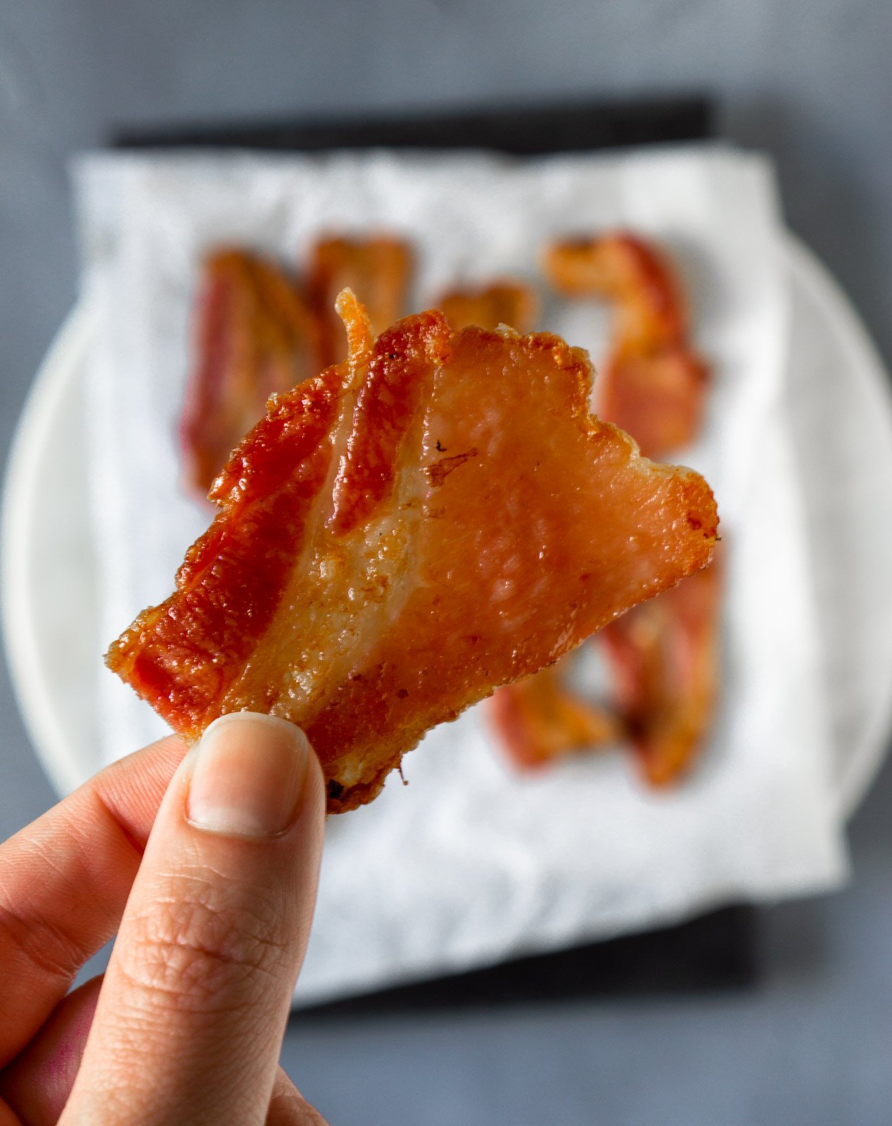 A hand holding a piece of air fryer bacon.