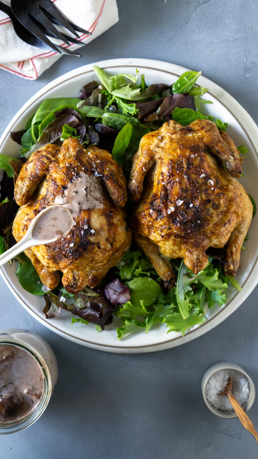 A white spoon pouring bacon gravy over a cornish hen on a plate.