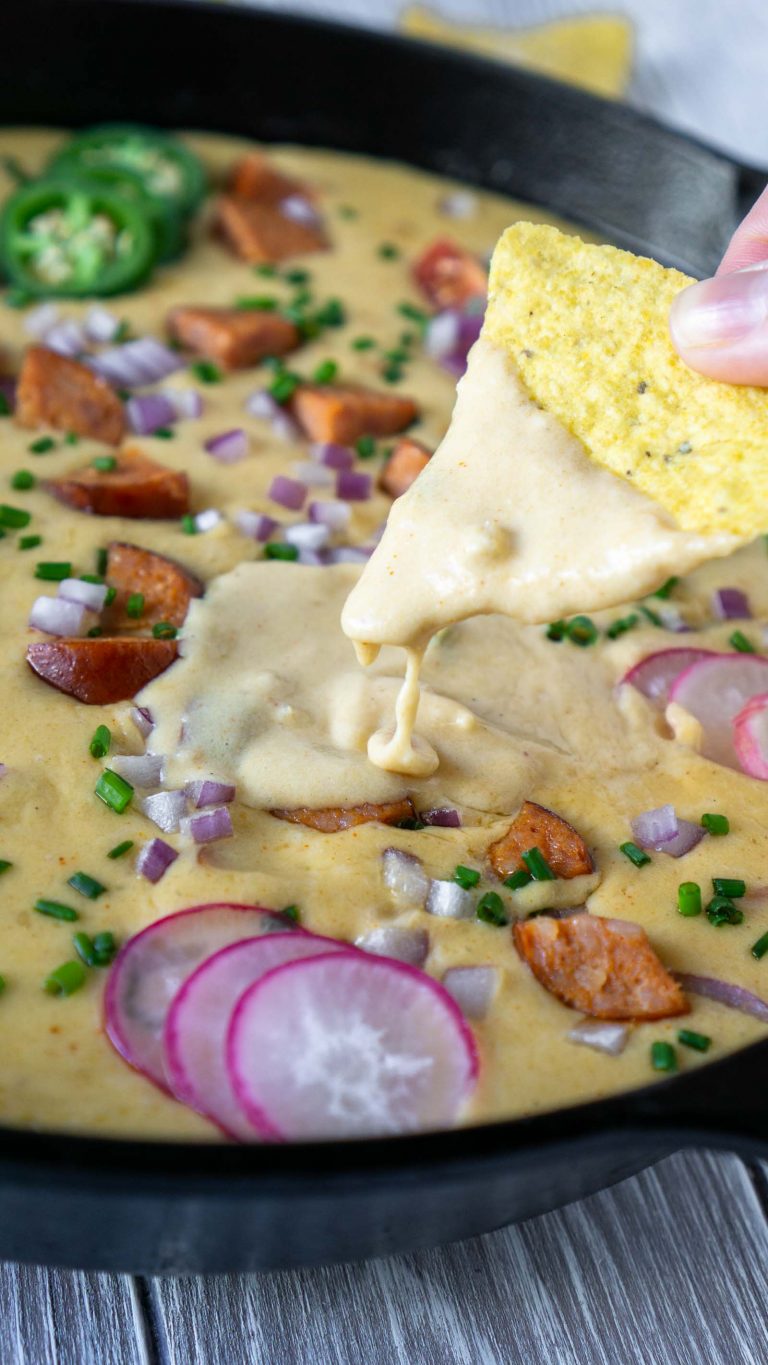 a hand dipping a chip in beer cheese