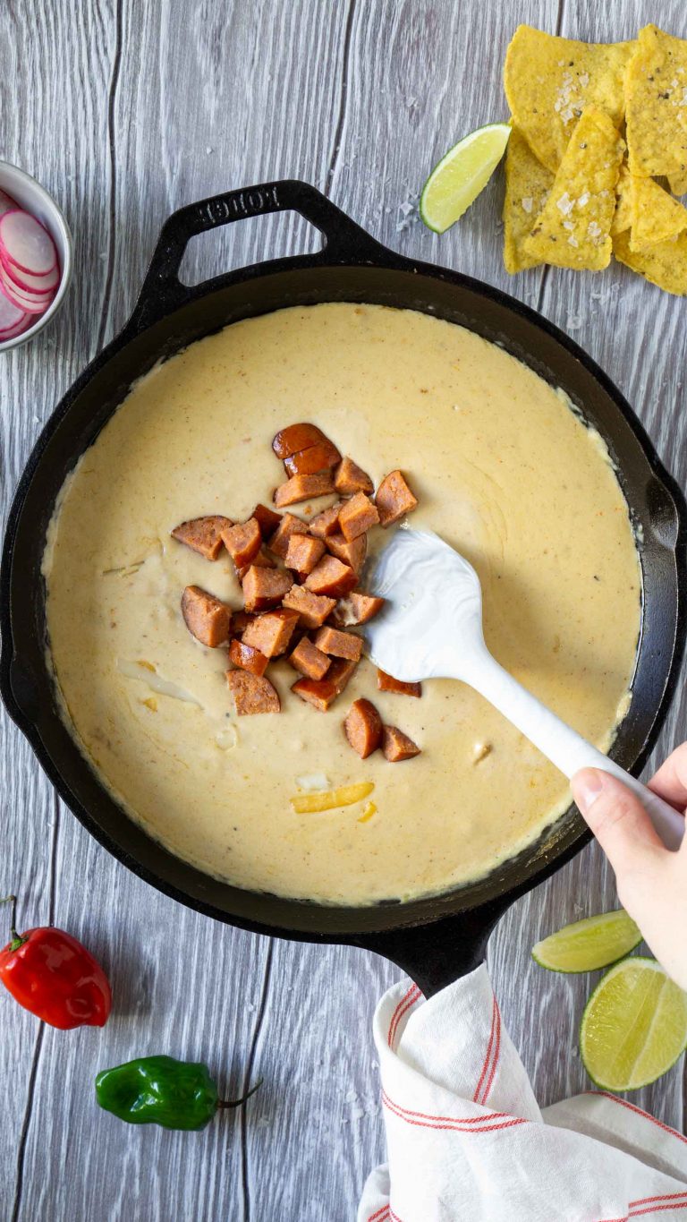 a hand mixing sausage into beer cheese dip with a white spatula