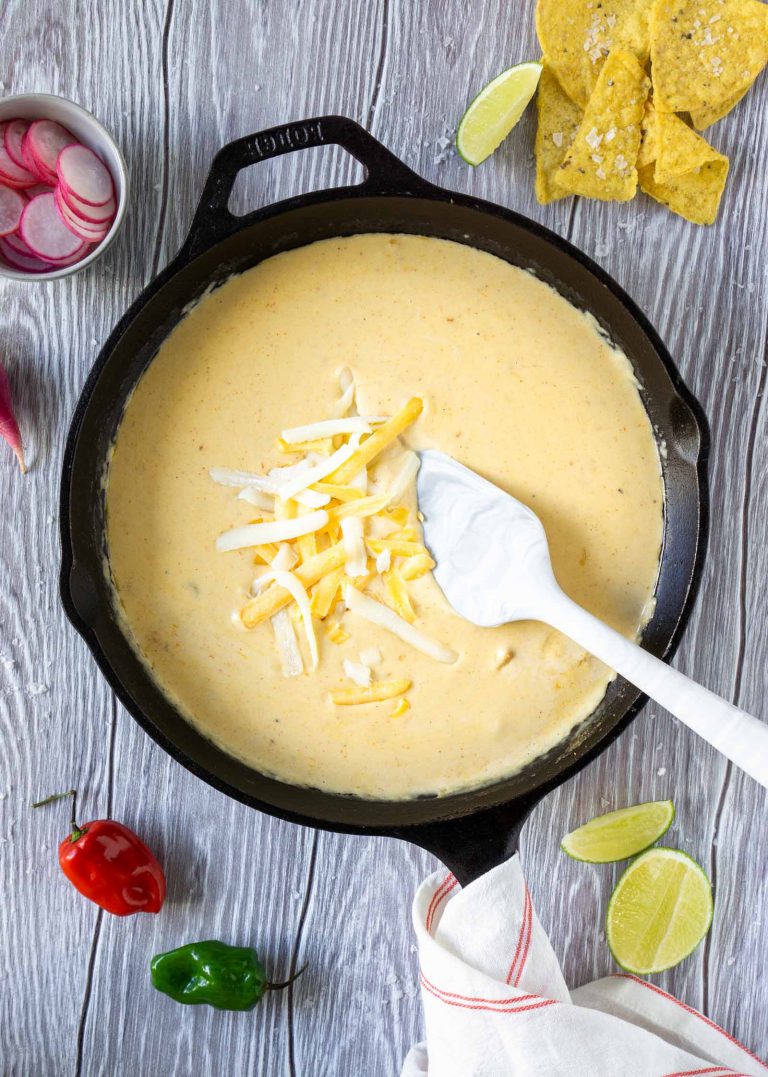 a white spatula mixing cheese into the dip in a cast iron skillet