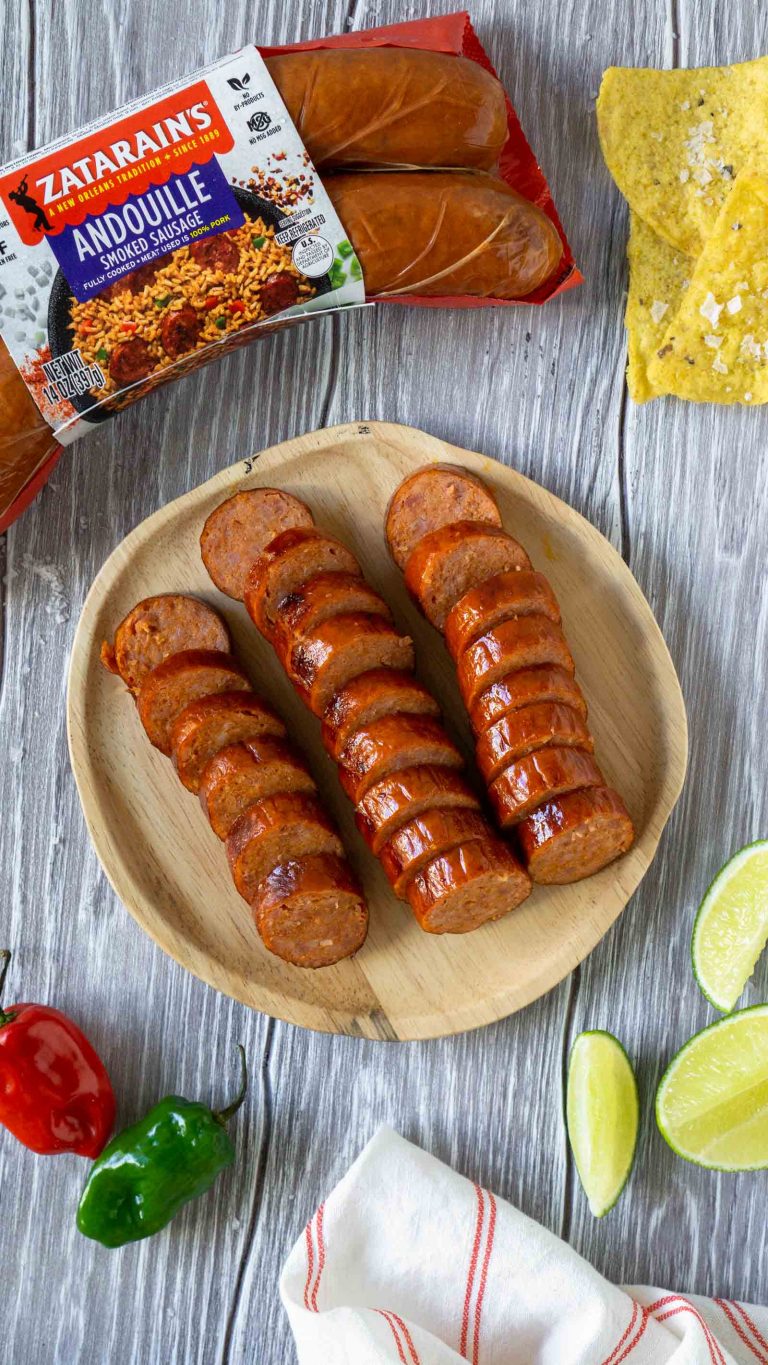 sliced sausage on a wooden plate with limes, chips, and spicy peppers