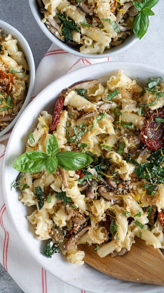 one large white bowl of tuscan kale pasta and two small bowls