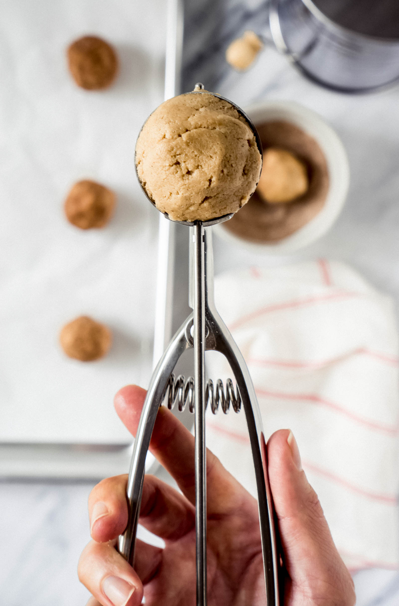 a hand holding a cookie scooper with a scoop of cookie dough