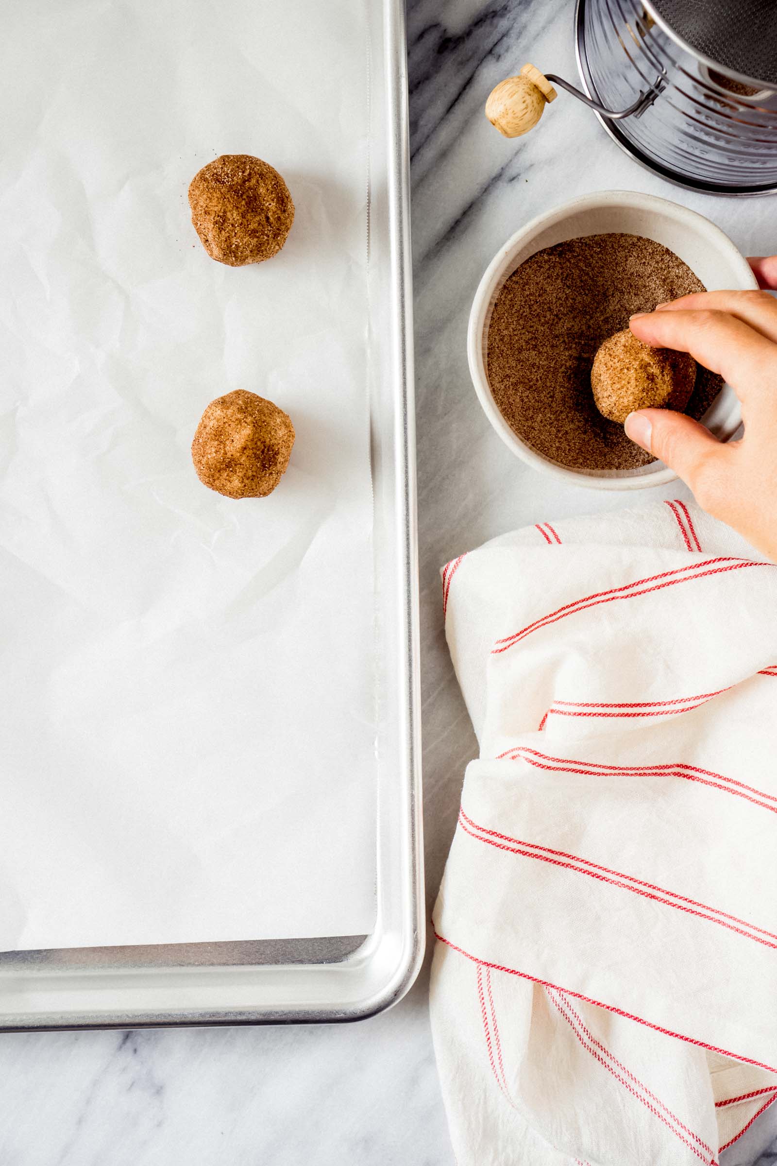 a hand rolling a cookie dough ball in cinnamon sugar