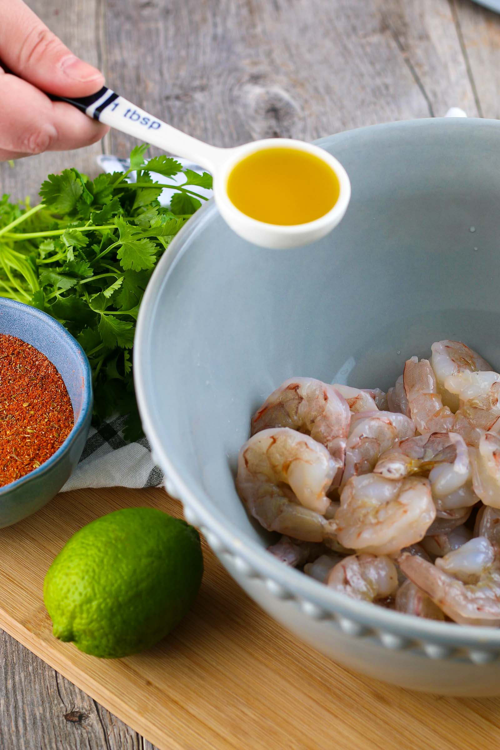 raw shrimp in a blue bowl and a tablespoon of olive oil