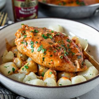 a white bowl with gnocchi and sun dried tomato pesto chicken and a jar of pesto in the background