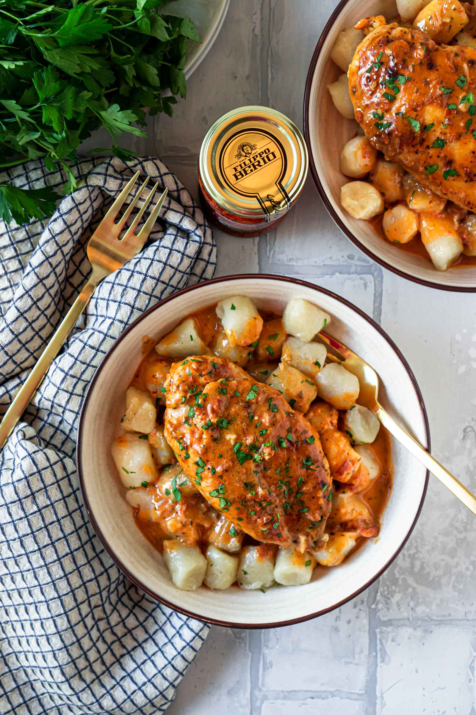 two bowls of creamy pesto chicken over cauliflower gnocchi with two gold forks