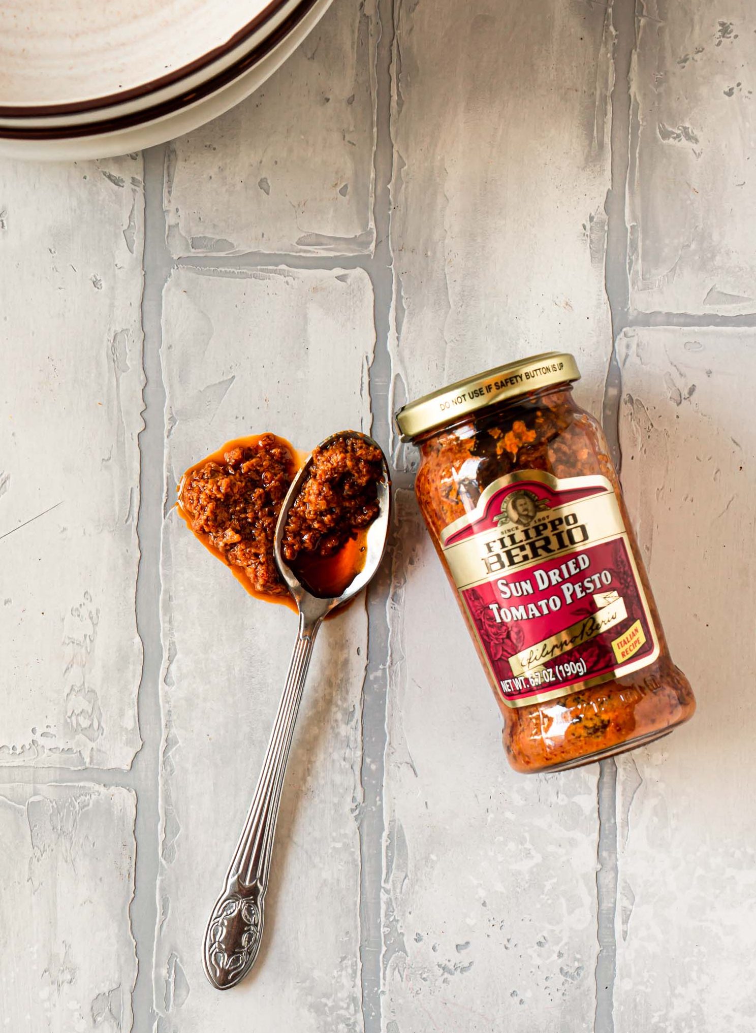 a jar of filippo berio sun dried tomato pesto and a silver spoon with pesto