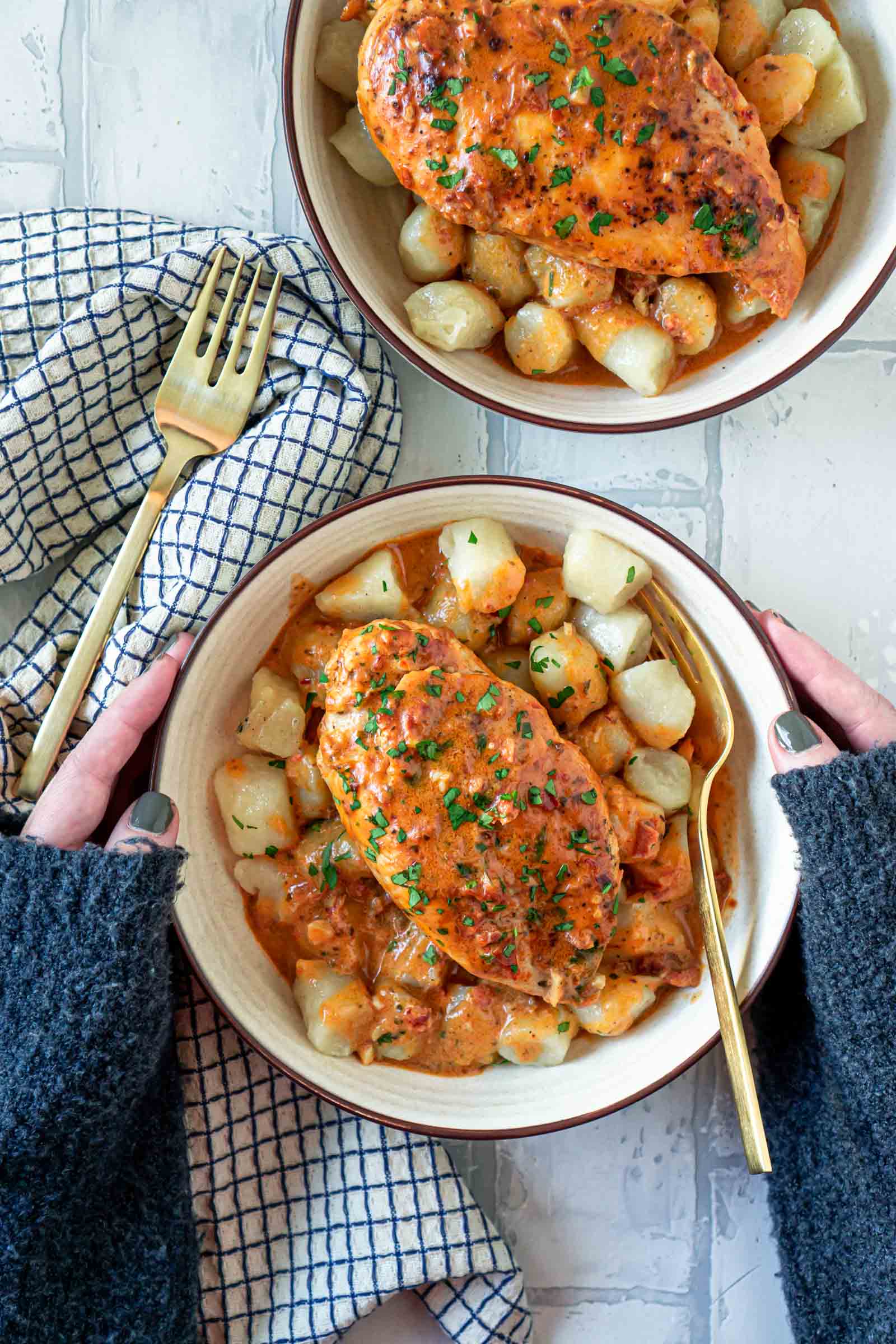two hands holding a bowl of cauliflower gnocchi and creamy pesto chicken
