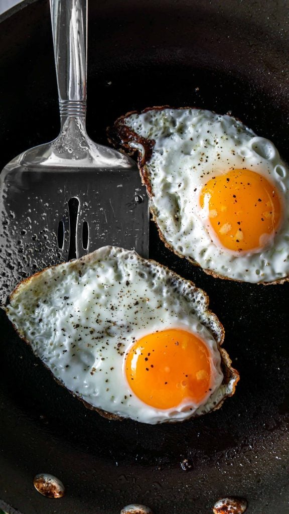 two fried eggs in a pan with a spatula