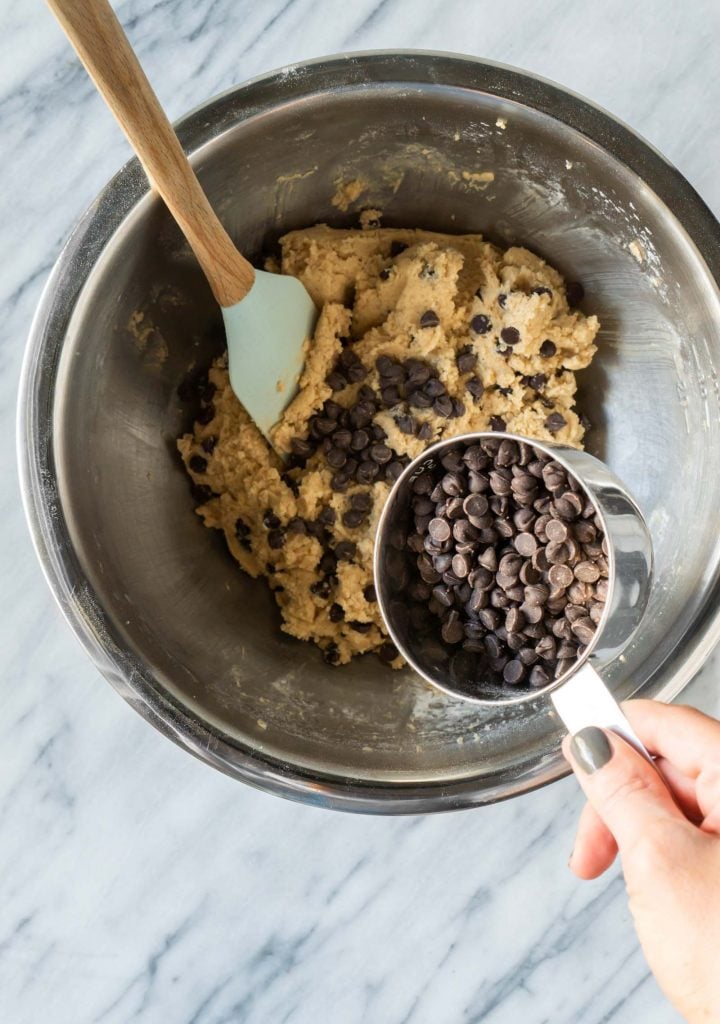 a hand pouring chocolate chips into the cookie dough