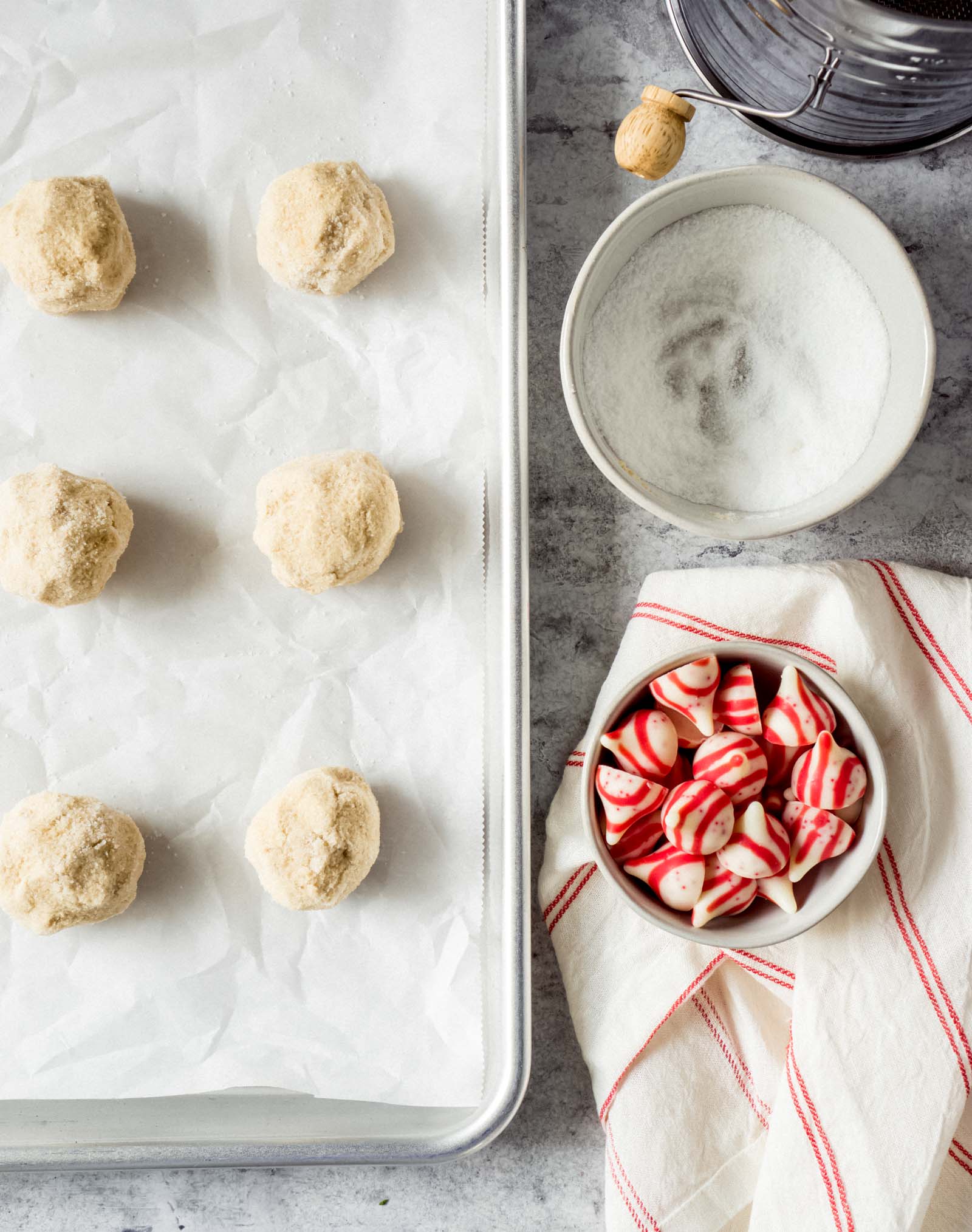 dough balls on a baking sheet with a bowl of candy cane kisses