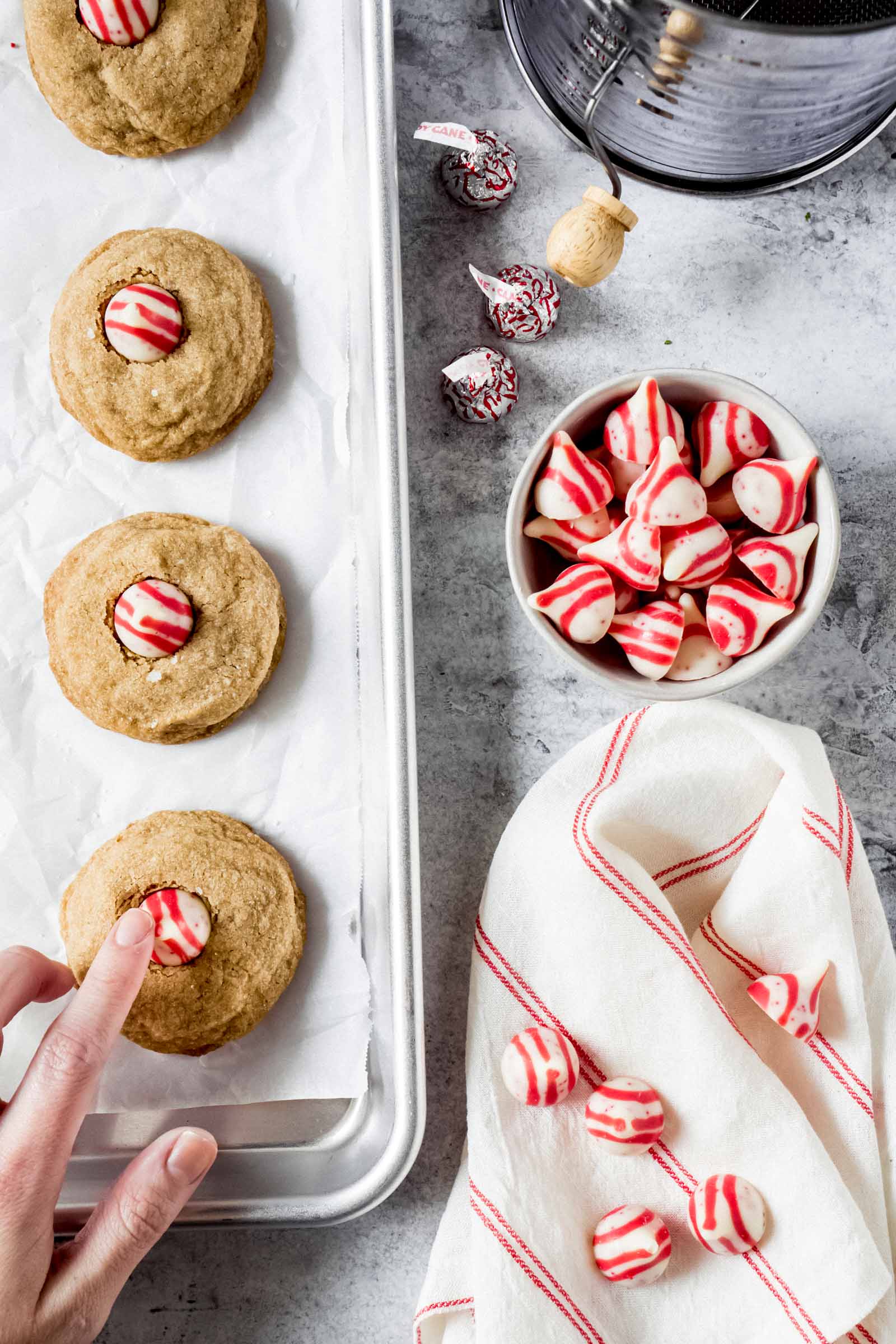 a hand pressing a candy cane hershey kiss into a cookie