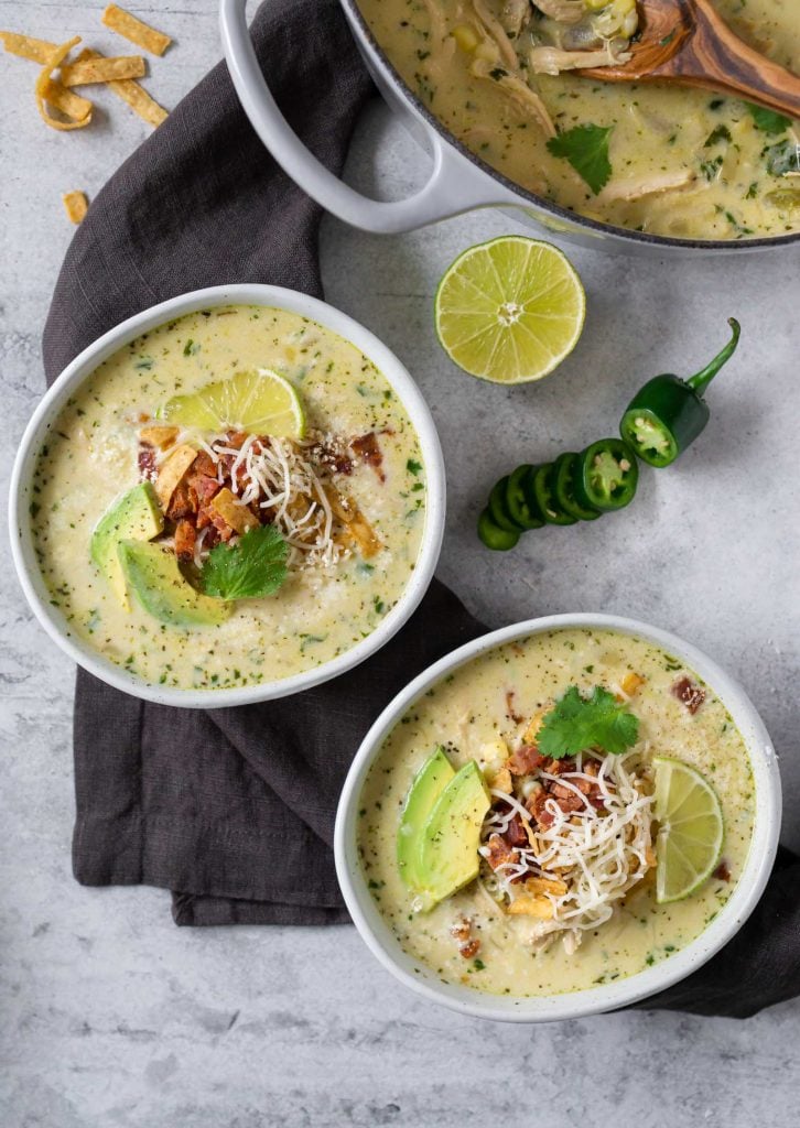 mexican street corn white chicken chili in two bowls with half a lime and a sliced jalapeno pepper