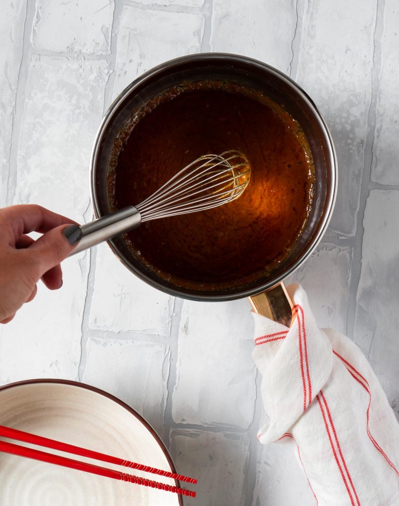 a hand holding a whisk over a pan with miso butter