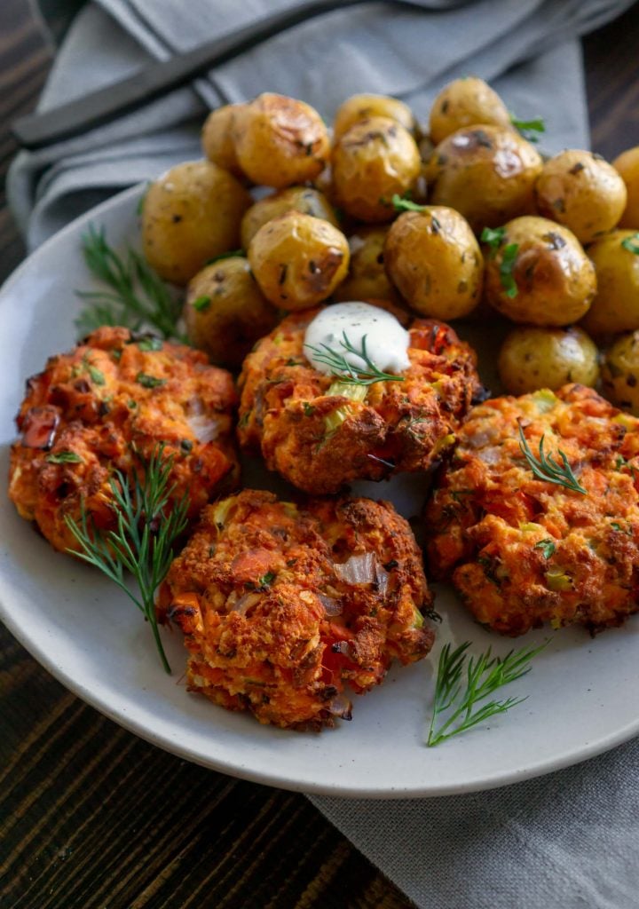 4 salmon cakes on a plate with roasted potatoes
