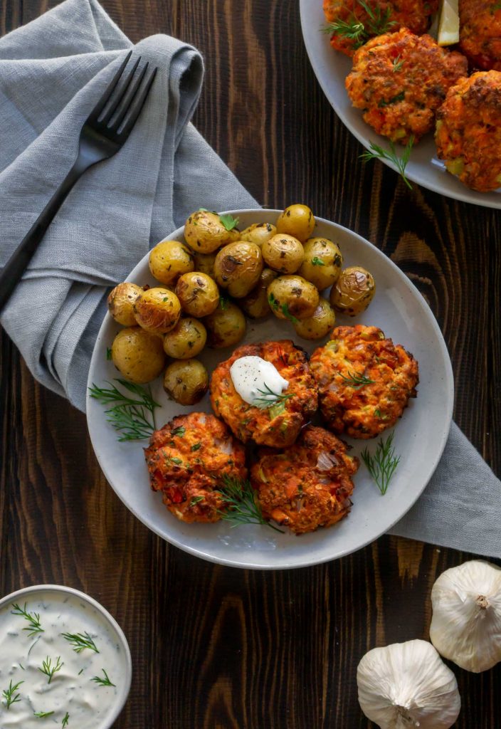 salmon cakes on a plate with potatoes, garlic and lemon dill sauce to the side