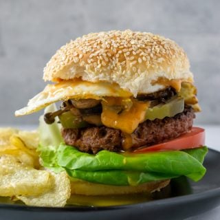 a wild mushroom burger on a black plate with chips