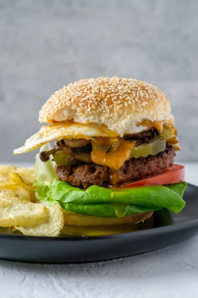 a wild mushroom burger on a black plate with chips