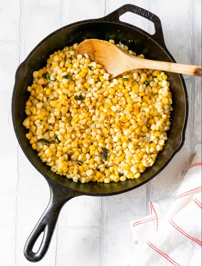 charred corn and jalapenos in a cast iron skillet with a wooden spoon