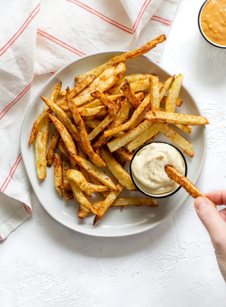 a hand dipping a french fry in mayonnaise