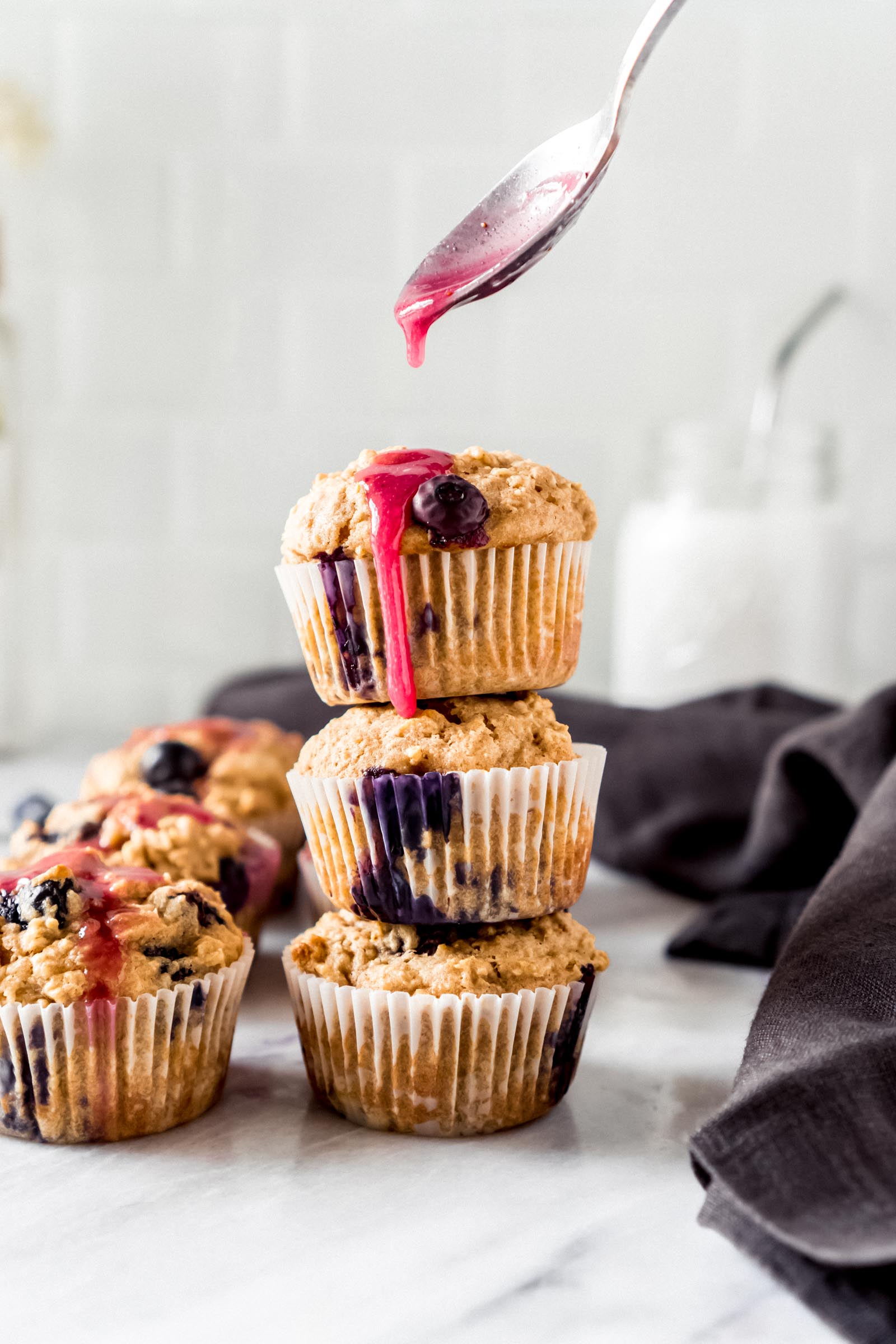 a spoon drizzling lemon blueberry glaze over oatmeal muffins