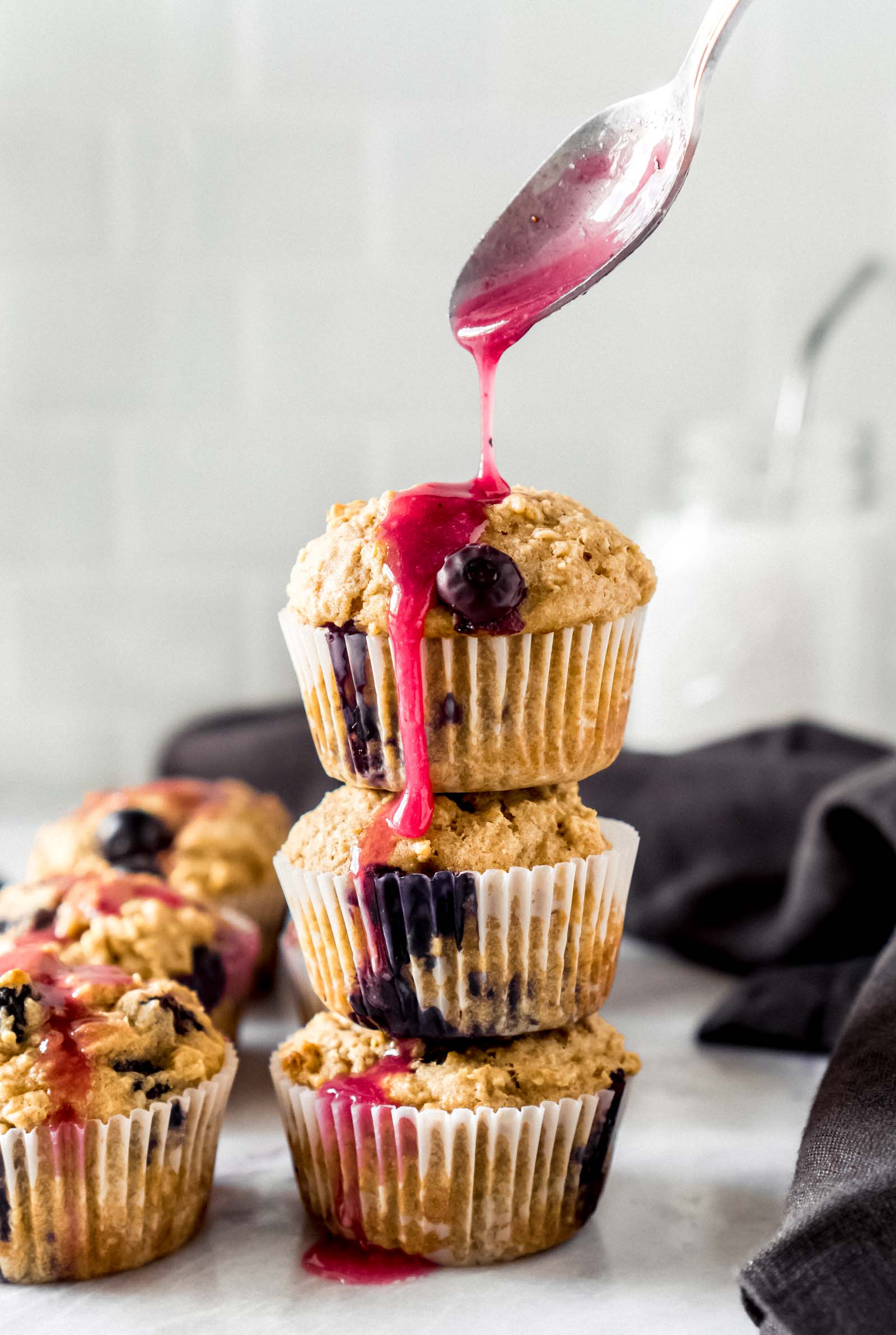 a spoon drizzling lemon blueberry glaze on oatmeal muffins