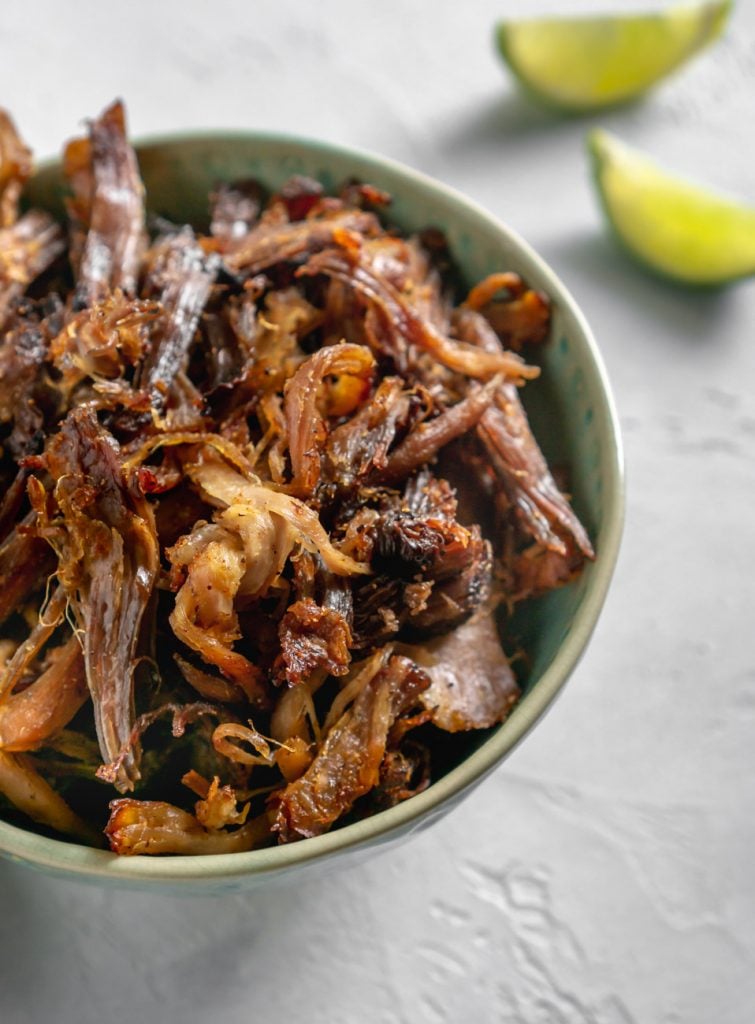 slow cooker carnitas in a bowl and two lime wedges