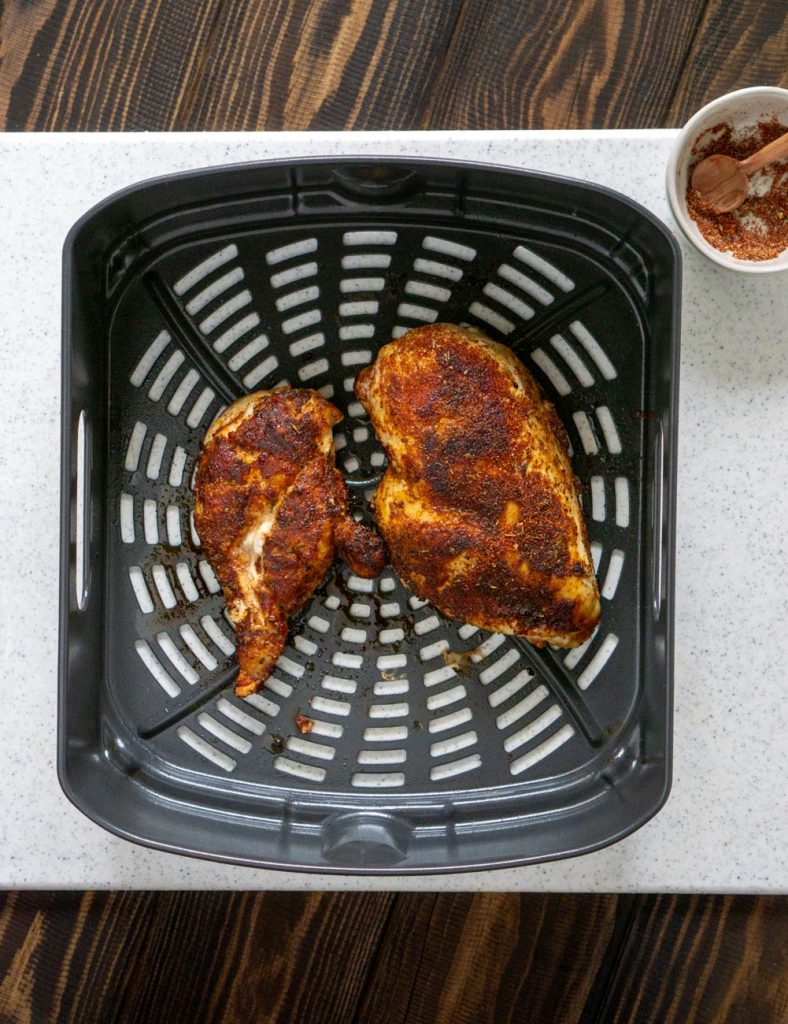 two cooked chicken breasts in an air fryer basket