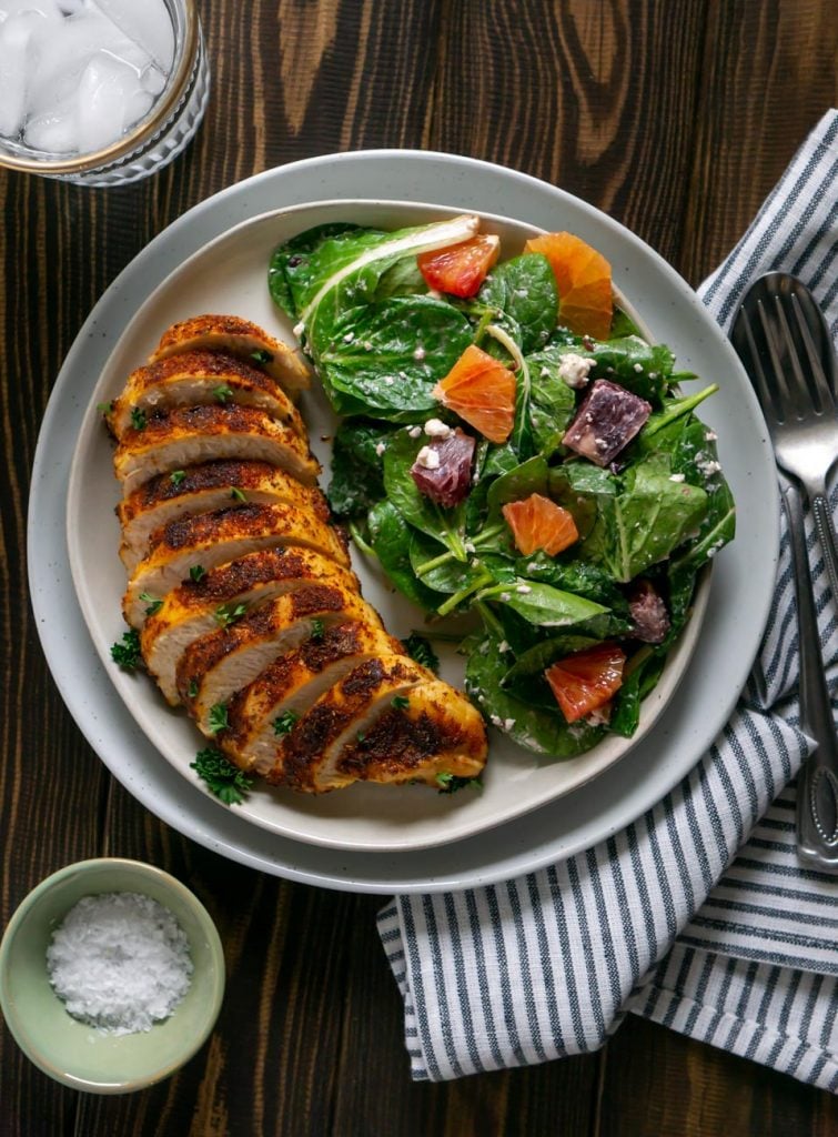 sliced air fryer chicken on a plate with salad and a glass of water