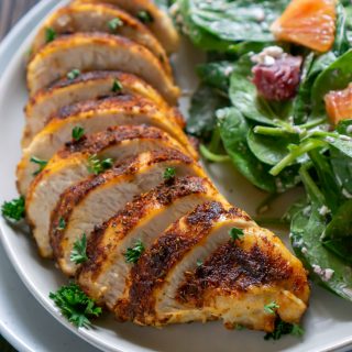 sliced air fryer chicken on a white plate with salad