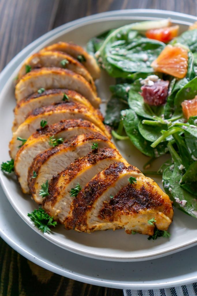 sliced air fryer chicken on a white plate with salad