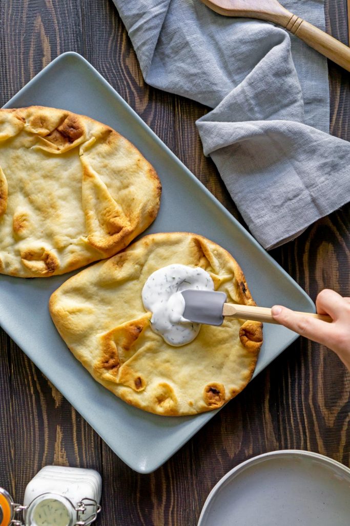 spatula spreading pizza sauce on naan