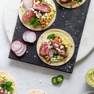 three steak tacos on a black slate board