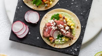 three steak tacos on a black slate board