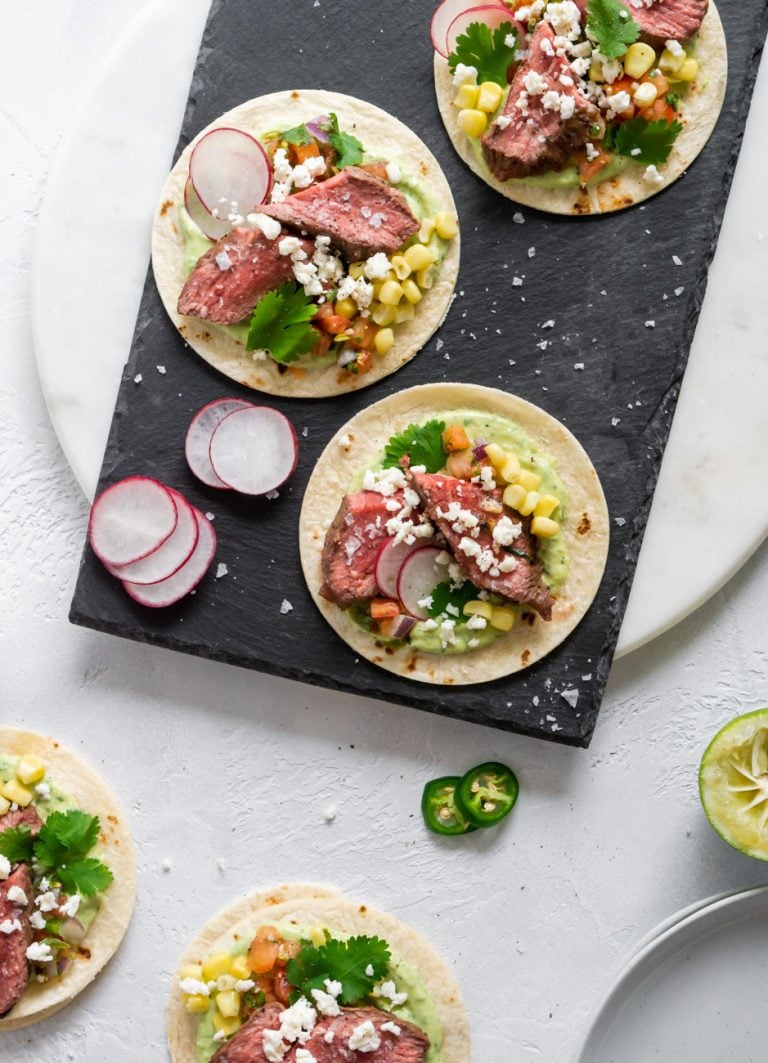 three steak tacos on a black slate board