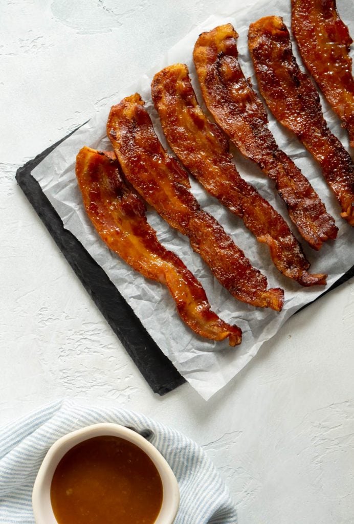 candied bacon on parchment paper next to maple glaze