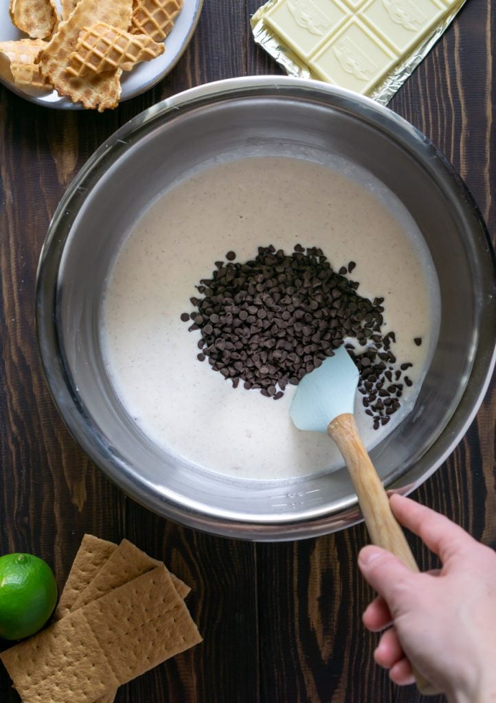 a spatula mixing chocolate chips into cannoli dip in a large metal mixing bowl