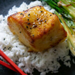 miso glazed chilean sea bass on a black plate with rice and red chopsticks