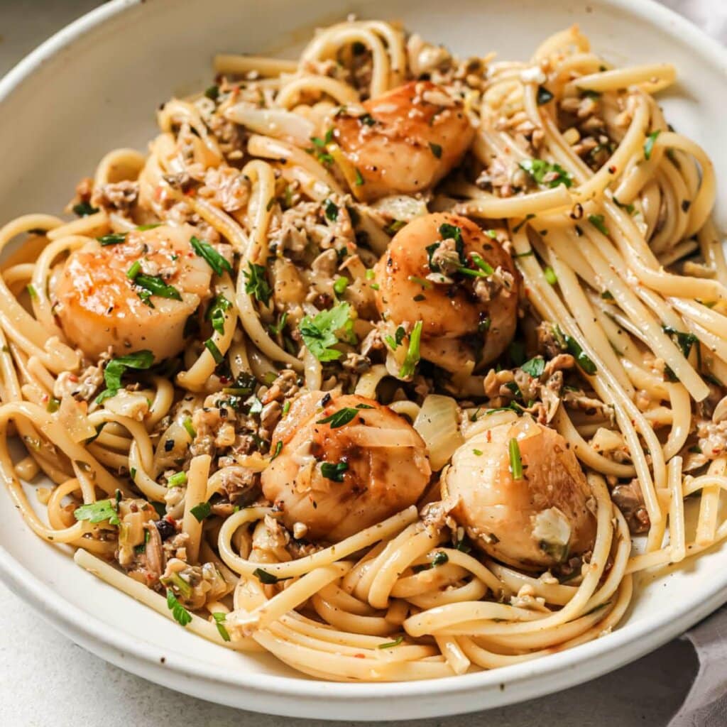 Linguine With Clam sauce in a white bowl topped with scallops