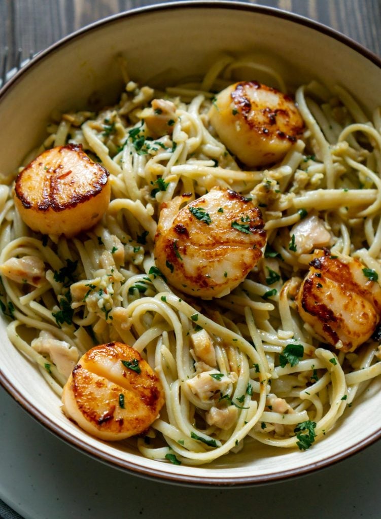 linguine with clam sauce and scallops in a white bowl on a wood table
