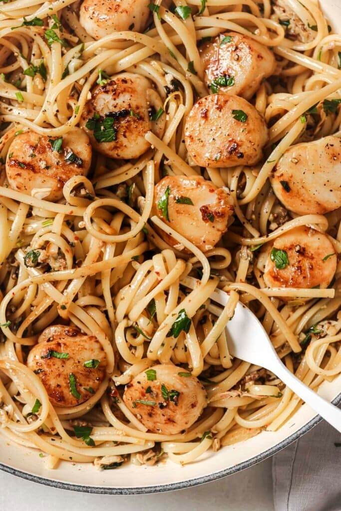 linguine with clam sauce in a large pan topped with scallops