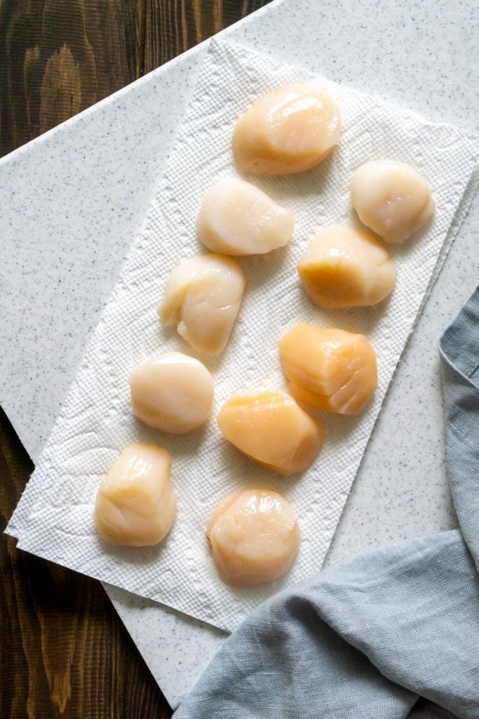 raw scallops on a paper towel and a white cutting board