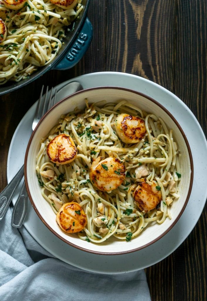 linguine with clam sauce and scallops in a white bowl with a fork